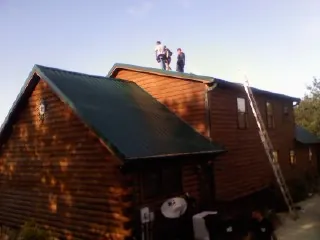 Crew on the ridge of a green metal roof on a two story log home in Springdale